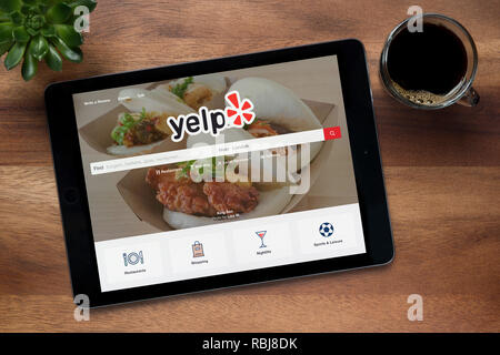 Die Website von Yelp ist auf einem iPad Tablet gesehen, auf einer hölzernen Tisch zusammen mit einem Espresso und einem Haus Anlage (nur redaktionelle Nutzung). Stockfoto