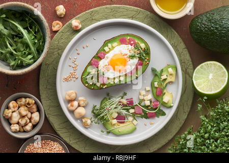 Keto Diät Teller: gebackene Avocado Boot mit Schinken würfeln, Wachtel Ei und Käse serviert mit grünen Rucola Salat, flach mit Zutaten Stockfoto