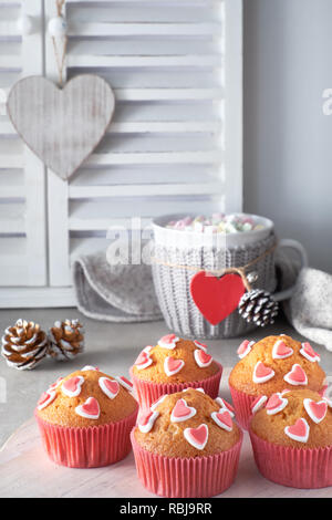 Muffins mit Zucker Herzen und eine Schale mit roten Herzen auf hellgrauem Hintergrund eingerichtet. Valentinstag oder Winter geburtstag Konzept. Stockfoto