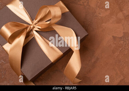 Ein Geschenk in einem Papier wird mit einem Satinband und Schleife auf braunem Hintergrund eingerichtet. Festliche Konzept. Flachbild Layout. Stockfoto