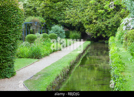 Wasser Kanal durch eine Kies Wanderweg in einem angelegten englischen Garten mit Bäumen, Sträuchern Formgehölze geformt, an einem Sommertag. Stockfoto