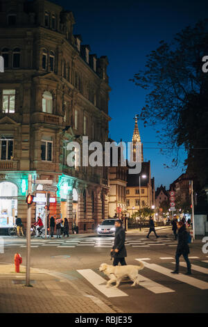 Straßburg, Frankreich - 31.Oktober 2017: Französische Straße Kreuzung überqueren - Straße mit Fußgänger Straße am Abend und Notre-Dame Kathedrale im Hintergrund beleuchtet - Mann, Hund Stockfoto