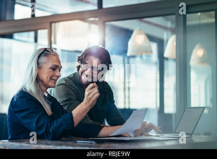 Geschäftsleute treffen sich im Büro und diskutieren über Dokumente. Geschäftsfrau mit einem Finanzbericht in der Hand, sitzt mit einem männlichen Kollegen, der schaut Stockfoto