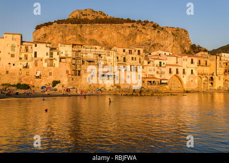 Blick auf die Altstadt von Cefalù bei Sonnenuntergang vom alten Hafen mit Häusern mit Blick auf die ruhige See. Stockfoto