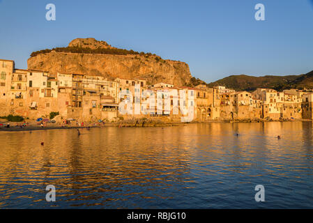 Blick auf die Altstadt von Cefalù bei Sonnenuntergang vom alten Hafen mit Häusern mit Blick auf die ruhige See. Stockfoto