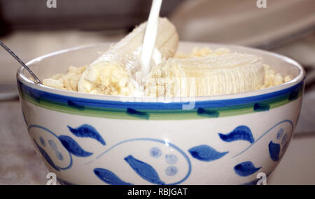 Milch in die Schüssel Müsli und Banane gießen Stockfoto