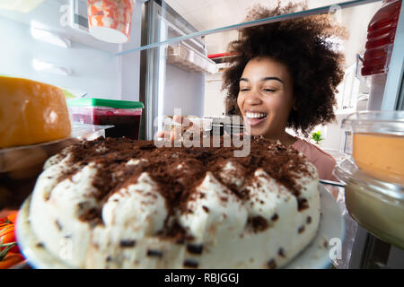 Junge Frau essen Kuchen aus dem Kühlschrank. Stockfoto