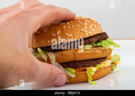 Nahaufnahme Bild der menschlichen Hand mit einem leckeren doppelten Cheeseburger mit Salat Stockfoto