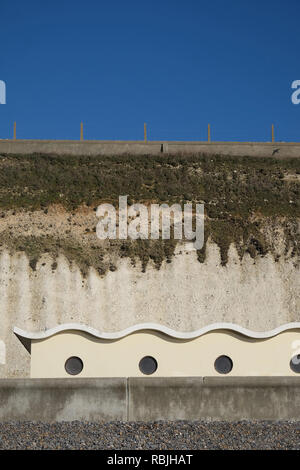 Ein Kiesstrand mit einer Betonmauer und hinter einer Reihe von vier im Art déco-Stil Strand Hütten mit Glas Bullaugen in jedem, der Strand Hütten sitzen an den Bot Stockfoto