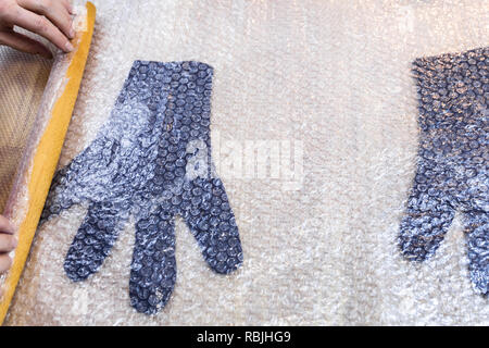 Werkstatt von Hand eine Fleece Handschuhe von blau Merino Schafschurwolle nass Filzen Prozess - Handwerker Brötchen gefilzte Handschuhe mit Holz- Rolling Pin Stockfoto