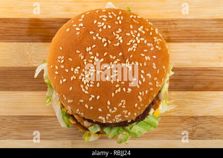 In der Nähe Bild von köstlichen doppelten Cheeseburger mit Rindfleisch, Cheddar und Salat in einem sesambrötchen. Ansicht von oben. Holz- Hintergrund Stockfoto