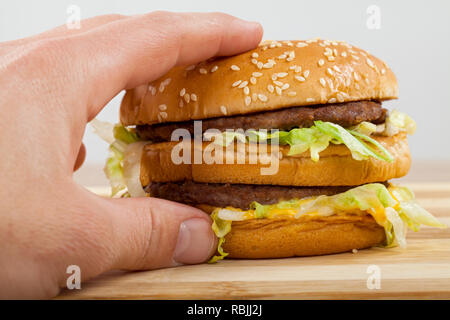 Nahaufnahme Bild der menschlichen Hand mit einem leckeren doppelten Cheeseburger mit Rindfleisch, Cheddar und Salat Stockfoto