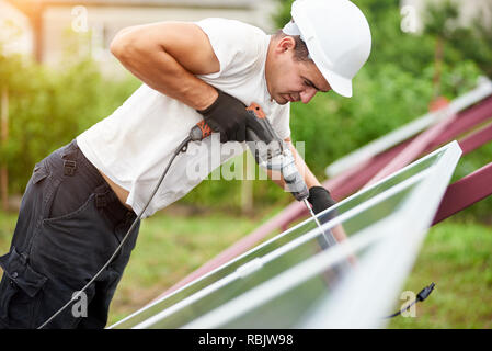 Profil von professionellen Techniker arbeiten mit Schraubendreher Connecting Solar Photovoltaik Panel zu Metall Plattform auf grüner Sommer verschwommene bokeh Hinterg Stockfoto