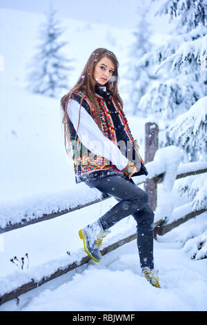 Junge attraktive Modische langhaarigen Frau in Jeans, weißes, traditionelles Ukrainischen bestickte Bluse und bunten Strickwesten bei einfachen Holz- Stockfoto