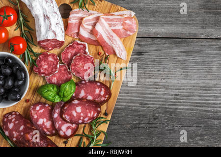 Essen Fach mit leckeren Salami, Speck, geräucherter Wurst, Oliven, Tomaten und Kräutern. Fleischplatte auf rustikalen Holztisch. Ansicht von oben mit der Kopie Raum Stockfoto