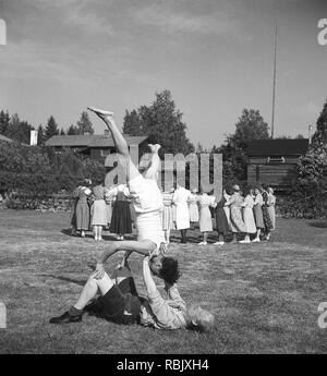 Sommer Tanz in den 1940er Jahren. Eine Gruppe von Frauen üben ihre ring Tanz an einem Outdoor Dance Event im Sommer. Zwei Männer im Vordergrund nicht an der Teilnahme interessiert erscheinen, und nicht ihre eigene Balance Akt, Unbekannt, warum. Foto Kristoffersson Ref 219-23. Schweden 1941 Stockfoto