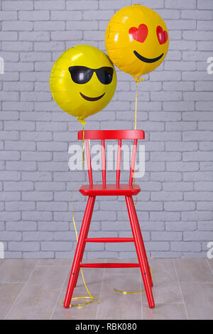 Grau Wohnung Studio mit Stuhl, Mauer, Gelb details Luftballons emoji roten Stuhl. Stockfoto