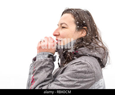 Mädchen, die versuchen, ihre Hände in einem Wintertag aufzuwärmen. Mädchen mit Schneeflocken in Haar im Winter Tag über dem weißen Himmel Stockfoto