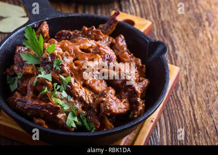 Stroganoff mit Tomatensauce und saure Sahne in Gusseisen Skillet auf rustikalen Holztisch serviert. Stockfoto