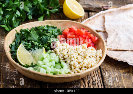 Tabbouleh salat Schüssel mit BULGUR, frische Petersilie, Tomaten, Gurken, serviert mit Pita-brot auf rustikalen Holztisch, selektiver Fokus, Nahaufnahme Stockfoto