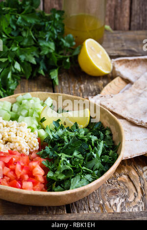 Tabbouleh salat Schüssel mit BULGUR, frische Petersilie, Tomaten, Gurken, serviert mit Pita-brot auf rustikalen Holztisch, selektiver Fokus, Nahaufnahme Stockfoto