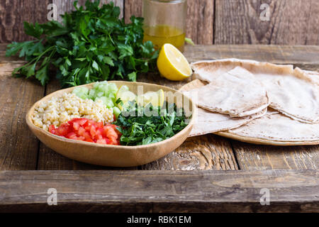 Tabbouleh salat Schüssel mit BULGUR, frische Petersilie, Tomaten, Gurken, serviert mit Pita-brot auf rustikalen Holztisch, selektiver Fokus, Nahaufnahme Stockfoto