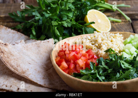 Tabbouleh salat Schüssel mit BULGUR, frische Petersilie, Tomaten, Gurken, serviert mit Pita-brot auf rustikalen Holztisch, selektiver Fokus, Nahaufnahme Stockfoto