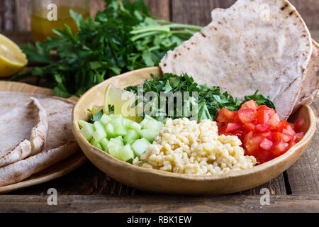 Tabbouleh salat Schüssel mit BULGUR, frische Petersilie, Tomaten, Gurken, serviert mit Pita-brot auf rustikalen Holztisch, selektiver Fokus, Nahaufnahme Stockfoto