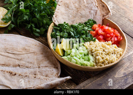 Tabbouleh salat Schüssel mit BULGUR, frische Petersilie, Tomaten, Gurken, serviert mit Pita-brot auf rustikalen Holztisch, selektiver Fokus, Nahaufnahme Stockfoto