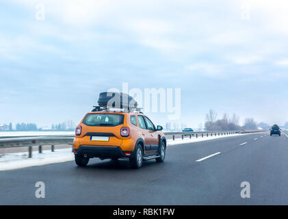 Orange Auto mit Dach Gepäckraum auf der Autobahn im Winter. Familie reisen Konzept Stockfoto