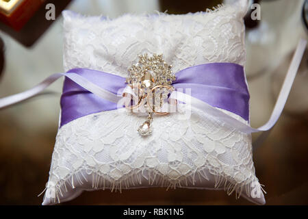 Ein paar Trauringe auf einem weißen Kissen. In der Mitte der Kissen ist ein Violettes Farbband. Ringe greift White Ribbon. Stockfoto