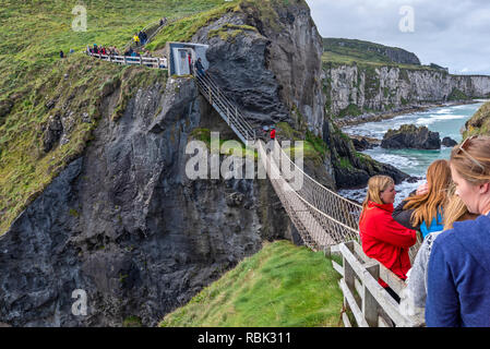 Touristen und Besucher erkunden und über die Hängebrücke zu Fuß bei Carrick-a-Rede und Larrybane Bay an der Westküste Irlands. Stockfoto