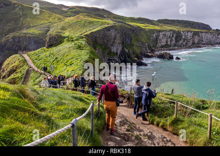 Touristen und Besucher erkunden und über die Hängebrücke zu Fuß bei Carrick-a-Rede und Larrybane Bay an der Westküste Irlands. Stockfoto