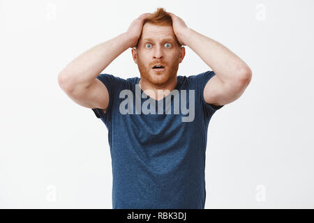 Was soll ich nun tun. Portrait von schockiert und verzweifelt attraktive Rothaarige mit Borsten,, Hände auf Haare, Augen und Ablegen von Kiefer von Schock und Verzweiflung, stehend über grauer Hintergrund Stockfoto