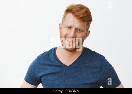 Unscheinbar ich besser tun können. Portrait von unzufrieden und enttäuscht , Stattlichen reifer Mann mit roten Haaren und runzelte die Stirn und starrte auf Kamera, Abneigung oder Zögern über graue Wand Stockfoto