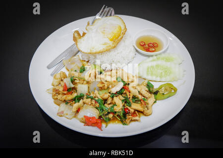 Gebraten heiß und würzig Thai Food/fried Heiliges Basilikum chicken Slice mit ein Ei Braten und Kochen von Reis auf dem Teller rühren - weil Fried Chicken Gurke und ch Stockfoto