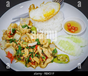 Gebraten heiß und würzig Thai Food/fried Heiliges Basilikum chicken Slice mit ein Ei Braten und Kochen von Reis auf dem Teller rühren - weil Fried Chicken Gurke und ch Stockfoto