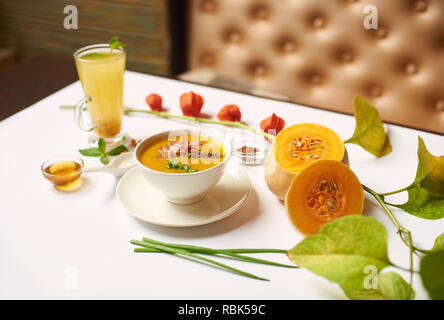 Kreative noch Leben diente auf dem Tisch für das Abendessen. Zarte creme Suppe und Kaffee in der Tasse im orientalischen Restaurant zubereitet. Grüne Blätter und die Hälften der Kürbis in der Nähe von Essen liegen auf weißen Tischdecke. Stockfoto