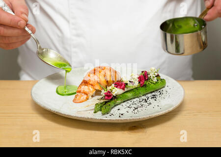 Koch gießen grüne Soße auf köstliche und nachhaltige Hummer, direkt vom Fischerboot auf den Tisch im Restaurant Stockfoto