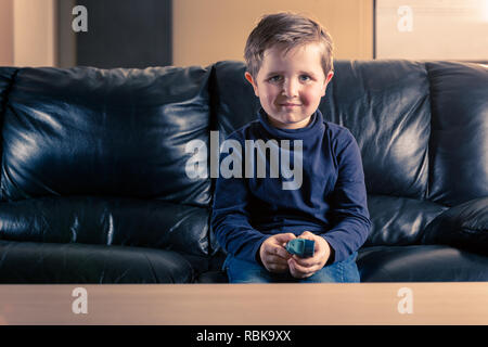 Süße 5 Jahre altes Kleinkind sein Asthma Inhalator sitzen in schwarzem Leder Sofa, während bei Camera suchen Holding Stockfoto