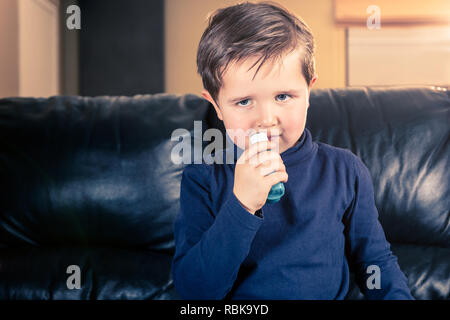 Süße 5 Jahre altes Kleinkind sein Asthma Inhalator sitzen in schwarzem Leder Sofa Holding Stockfoto