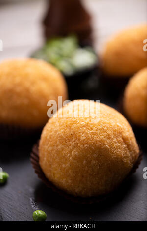 Nahaufnahme von arancini Reis Fleisch Ball Teller schwarz Servierteller mit frischen Erbsen und Basilikum auf rustikalen Tisch. Stockfoto