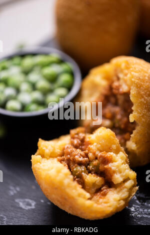 Nahaufnahme von arancini Reis Fleisch Ball Teller schwarz Servierteller mit frischen Erbsen und Basilikum auf rustikalen Tisch. Stockfoto