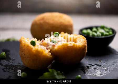 Nahaufnahme von arancini Reis Fleisch Ball Teller schwarz Servierteller mit frischen Erbsen und Basilikum auf rustikalen Tisch. Stockfoto