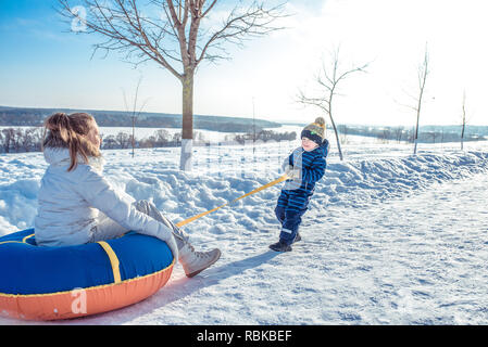 Mutter mit ihrem kleinen Sohn 3 Jahre alt, Reitschule Schläuche an einem sonnigen Tag in der Stadt im Winter. Spielen, Schnorcheln. Happy Scrabing Erholung in der Natur. Glückliche Familie an der frischen Luft. Stockfoto