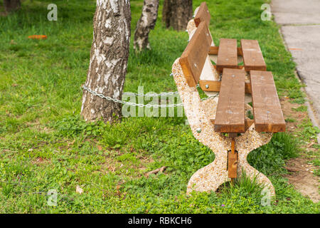 Eine eiserne Kette befestigt, eine Holzbank an einer geschäftigen Straße. Holz- sitz in der Straße mit einer eisernen Kette. Stockfoto