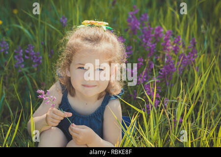 Süße blonde junge Mädchen stilvoll gekleidet in Blue Jeans Kleid posiert auf Wiese Wald wild mayweed. Wunderschön Szene. Stockfoto