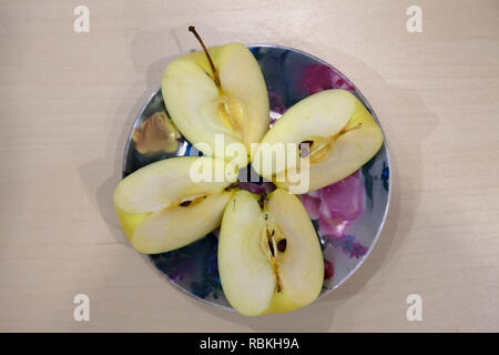Ein grüner Apfel schneiden in vier Stücke auf eine farbige Platte nach der Ernte im Herbst. Frisches Obst, Saft. Stockfoto