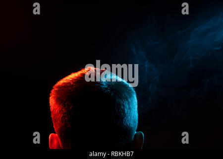Ein Blick von hinten auf den Kopf eines Mannes in einem T-Shirt Rauchen eine vape und Ausatmen mehrfarbige Rauch von Grün an verschiedenen Richtungen von sich selbst auf Stockfoto