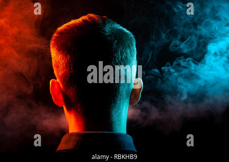 Ein Blick von hinten auf den Kopf eines Mannes in einem T-Shirt Rauchen eine vape und Ausatmen mehrfarbige Rauch von Grün und Rot in verschiedenen Richtungen von ihm Stockfoto